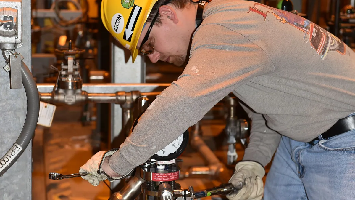 Maintenance worker tightening a pipe valve with a wrench on an industrial piping run