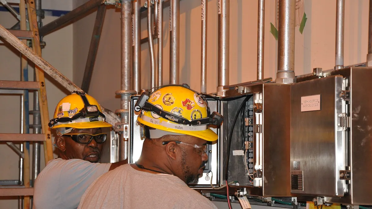 Two technicians inspecting an open electrical control cabinet on skid equipment
